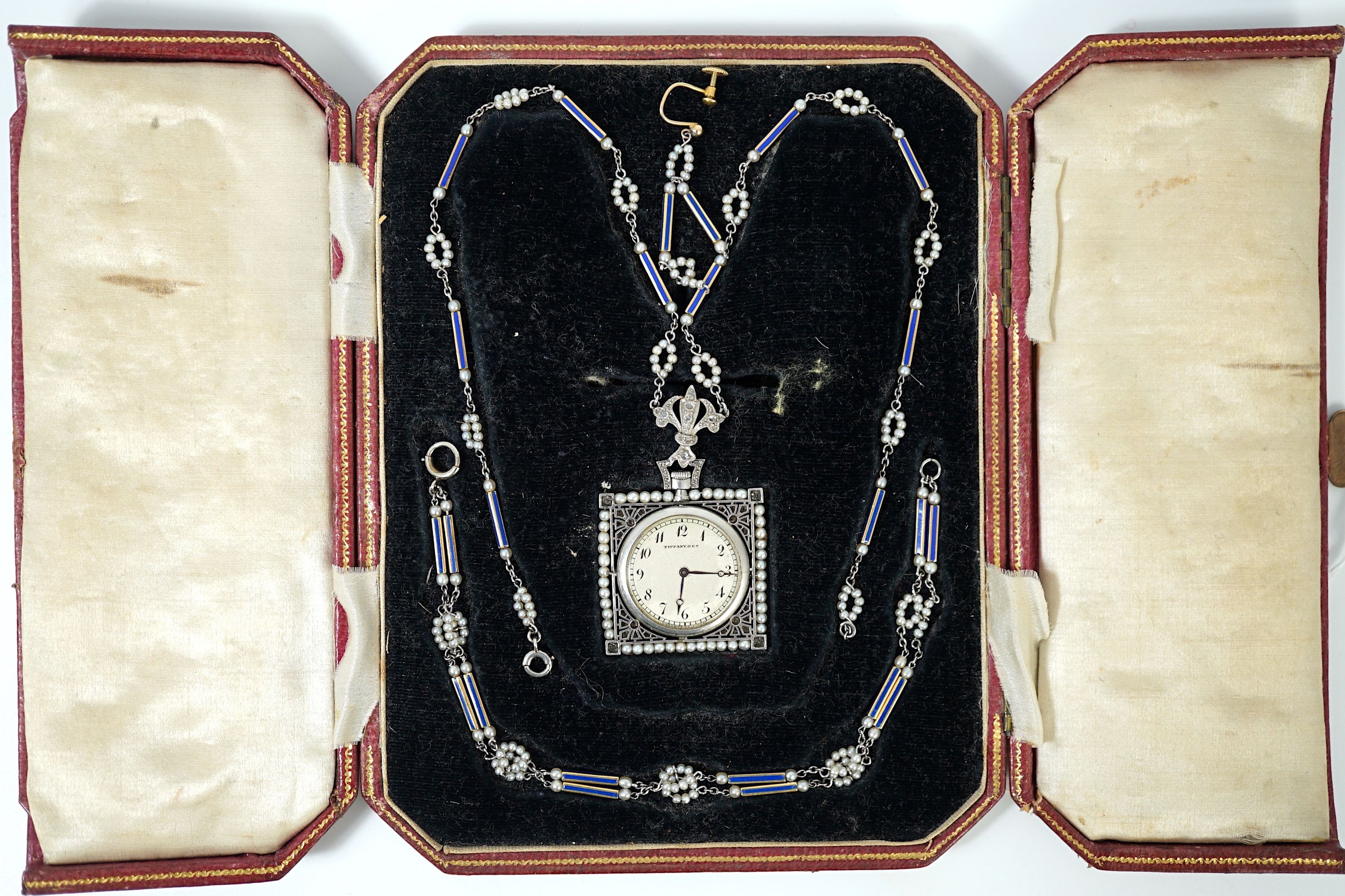 An early 20th century Tiffany & Co platinum, seed pearl and diamond set pendant square open faced dress timepiece, on a platinum, gold, enamel and seed pearl set chain, together with a matching 9ct bracelet and 9ct earri